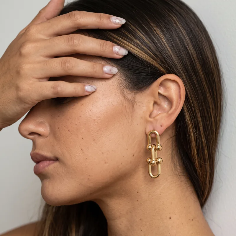 Gold link earrings worn, the model’s hand over her eyes, generated from a cut-out