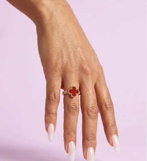 A clover ring on a hand against a lilac studio backdrop — product-only, one direction for the range